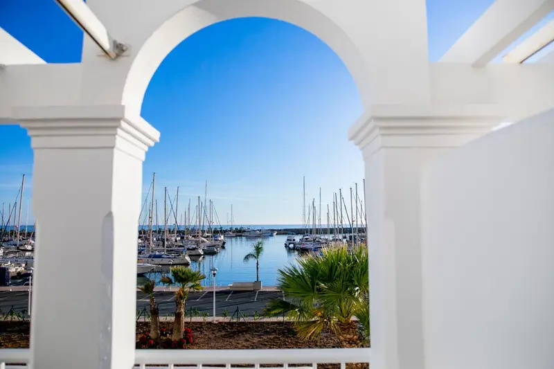 Vue sur un port de plaisance ensoleillé à travers une arche blanche.
