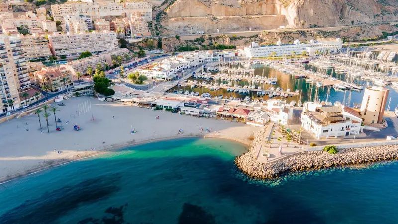 Vue aérienne d'une plage bordée de bâtiments et d'un port de plaisance.