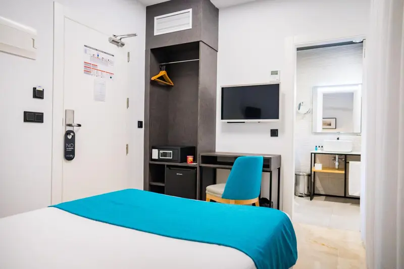 Une chambre lumineuse avec un lit turquoise et un bureau.
