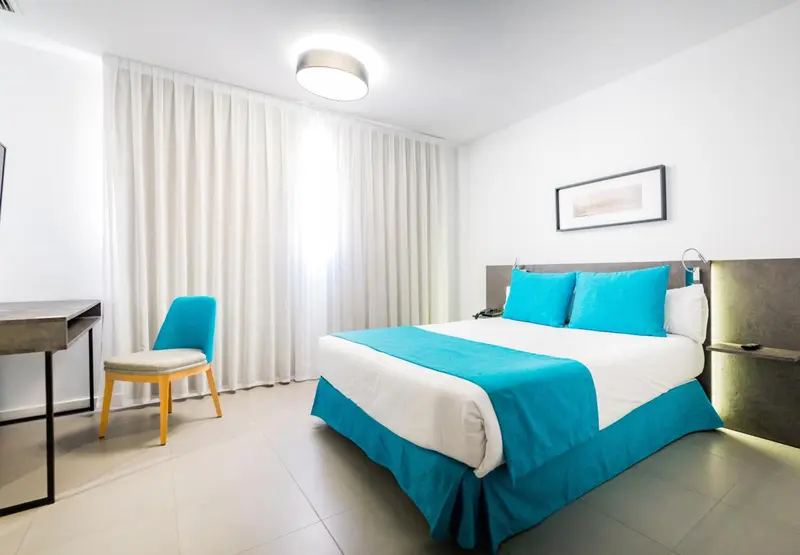 Une chambre lumineuse avec un lit turquoise et une chaise.