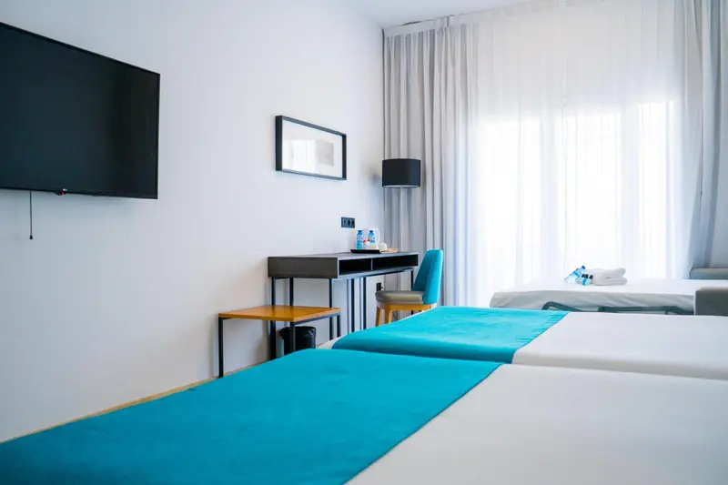 Une chambre avec deux lits turquoise et un bureau.