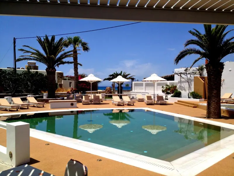 Une piscine turquoise reflète le ciel bleu, entourée de chaises longues et de palmiers.