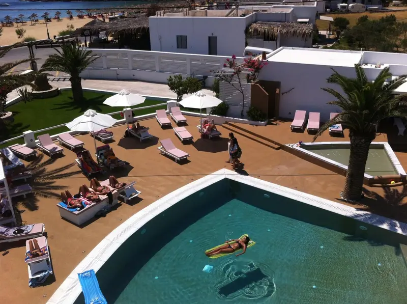 Vue aérienne d'une piscine avec des transats et des parasols sur une terrasse ensoleillée.