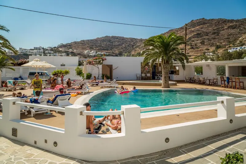 Une piscine ensoleillée avec des transats et des parasols, entourée d'une terrasse et d'une végétation luxuriante.