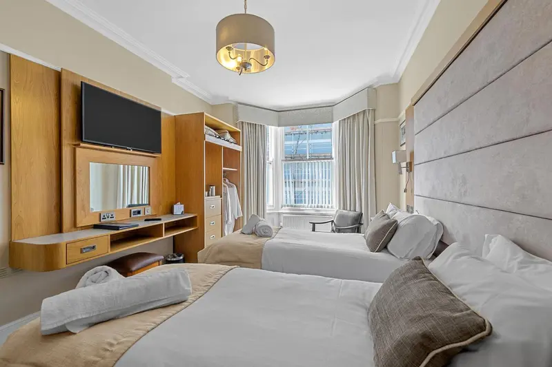 Chambre lumineuse avec deux lits simples et un coin salon près de la fenêtre.