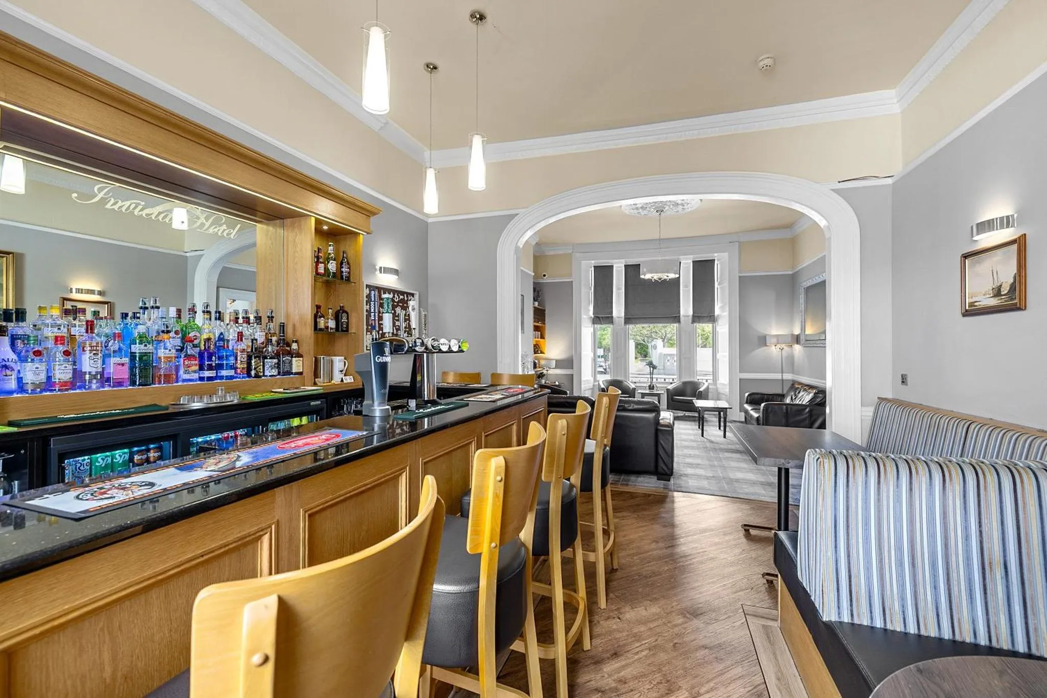 Un bar lumineux avec des tabourets et une sélection de boissons, donnant sur un espace salon.