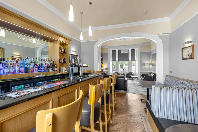Un bar lumineux avec des tabourets et une sélection de boissons, donnant sur un espace salon.