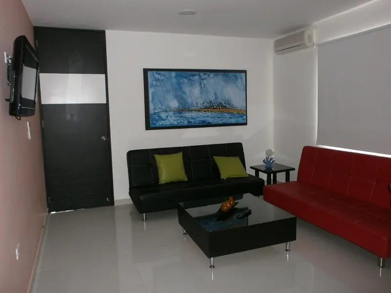 Un salon moderne avec canapés noirs et rouges, une table basse et un téléviseur mural.
