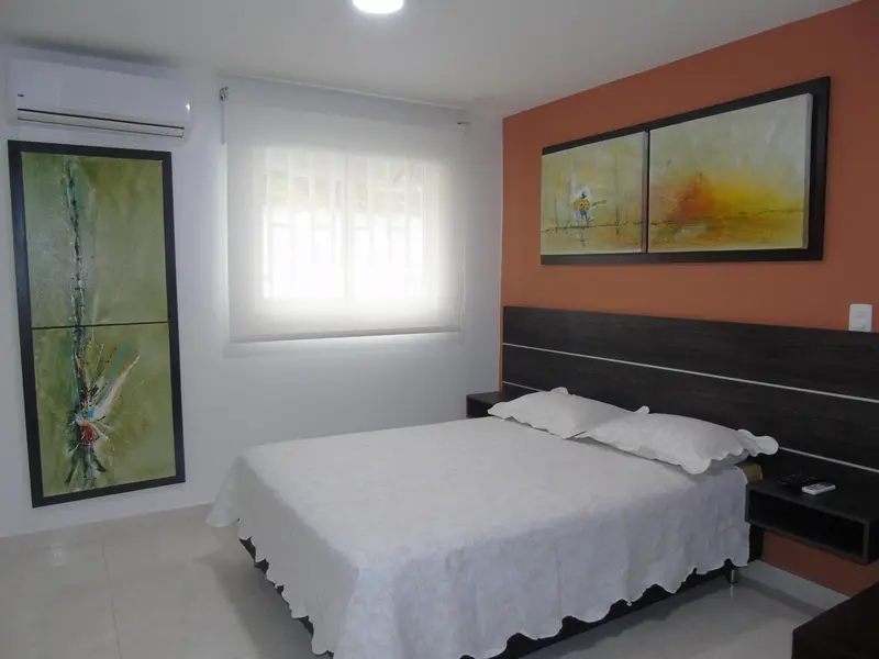 Une chambre lumineuse avec un lit recouvert d'une courtepointe blanche et des tableaux abstraits au mur.
