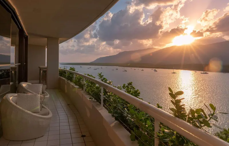 Terrasse avec mobilier blanc offrant une vue sur la mer et les montagnes au coucher du soleil.