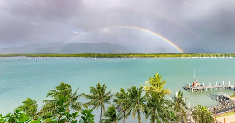Un arc-en-ciel se dessine au-dessus d'une baie abritant des bateaux à voile et un ponton.