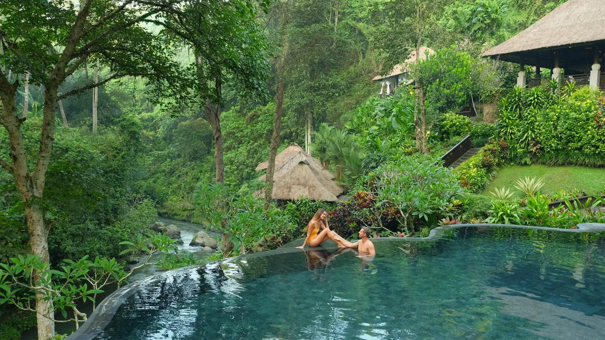 Un couple se détend au bord d'une piscine à débordement dans un cadre tropical luxuriant.
