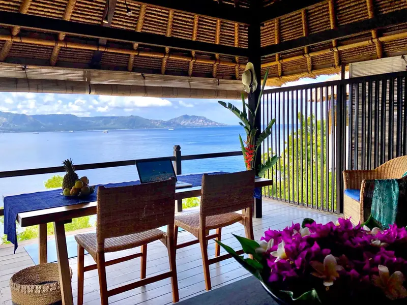 Une table et des chaises en rotin sont disposées sur une terrasse en bois avec vue sur la mer.
