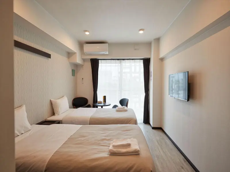 Chambre lumineuse avec deux lits simples et accès à une baie vitrée.