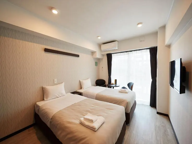 Une chambre lumineuse avec deux lits simples et un coin repas près de la fenêtre.