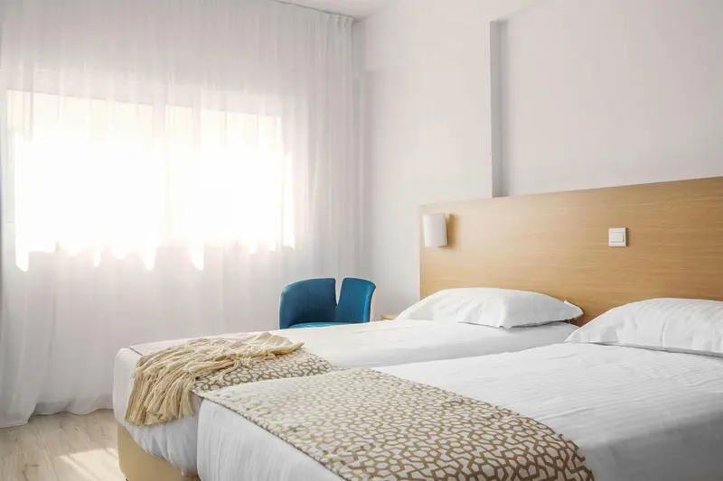 Une chambre lumineuse avec deux lits simples et un fauteuil bleu.
