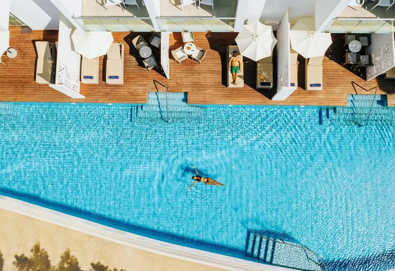 Terrasse en bois avec transats blancs et piscine turquoise.
