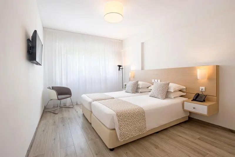 Une chambre lumineuse avec deux lits simples et un fauteuil.