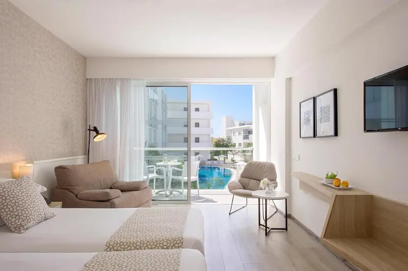 Une chambre lumineuse avec un coin salon et vue sur une piscine.