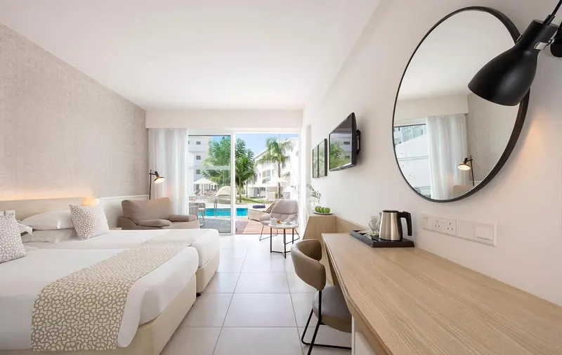 Chambre lumineuse avec un lit double, un coin salon et une vue sur la piscine.
