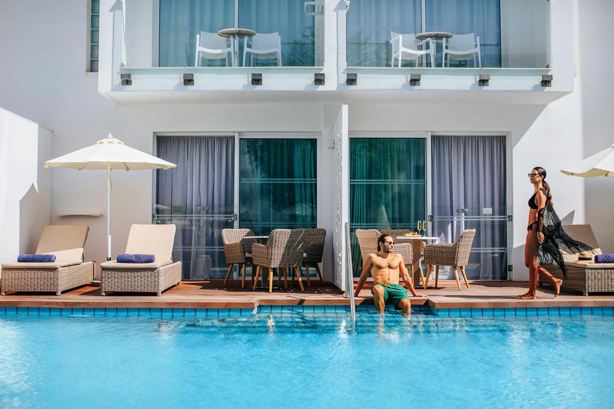 Une piscine bordée de transats et de parasols, avec des personnes se relaxant au soleil.