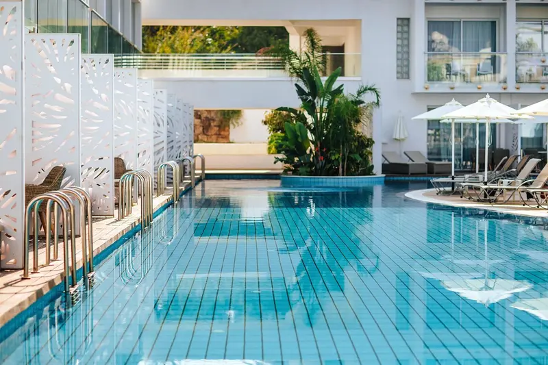 Une piscine rectangulaire turquoise bordée de chaises longues et de parasols.