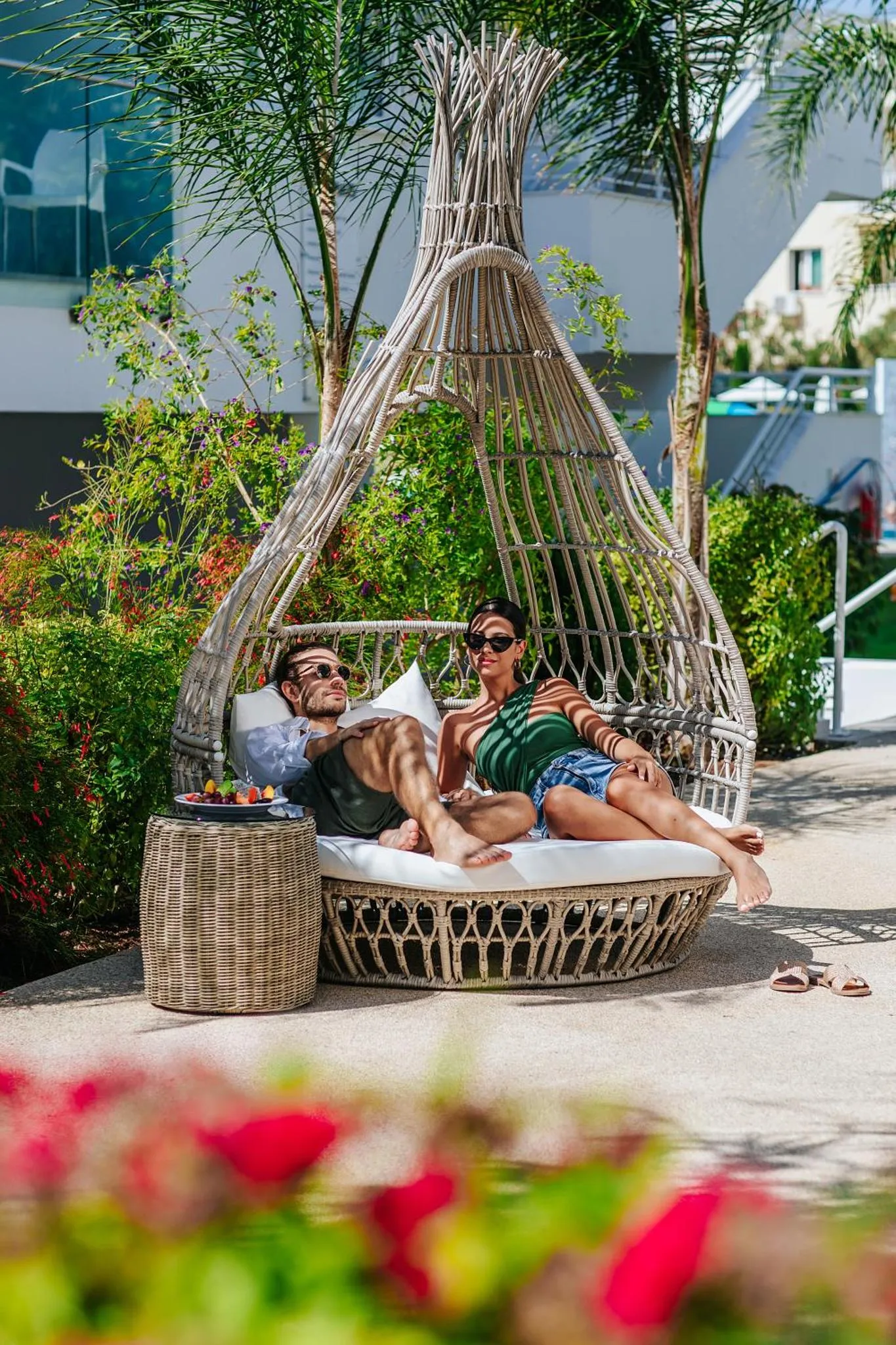 Deux personnes se reposent sur des coussins dans une structure en osier au bord d'une piscine.