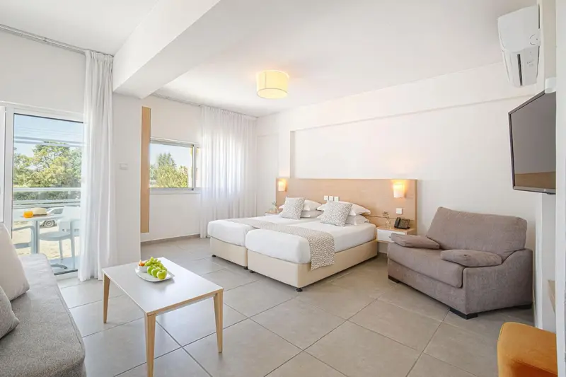 Chambre lumineuse avec un lit double, un canapé et un accès à un balcon.