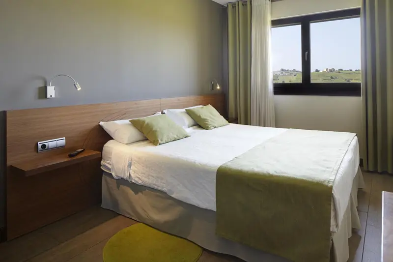 Une chambre lumineuse avec un grand lit recouvert d'une couette blanche et de coussins verts.