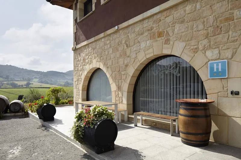 Terrasse fleurie devant un bâtiment en pierre avec des ouvertures arquées.