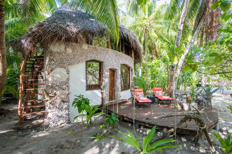 Une habitation de style cabane en bois et coquillages s'ouvre sur une terrasse en bois.