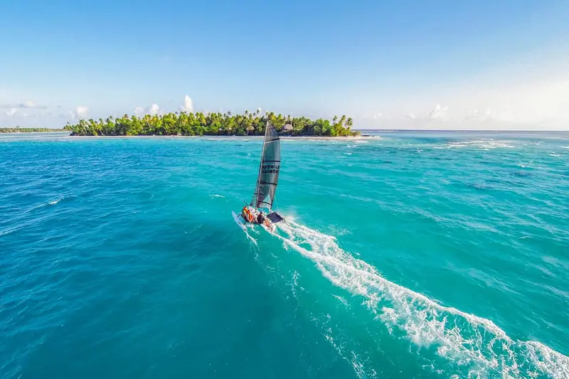 Un catamaran navigue sur une eau turquoise face à une île tropicale.