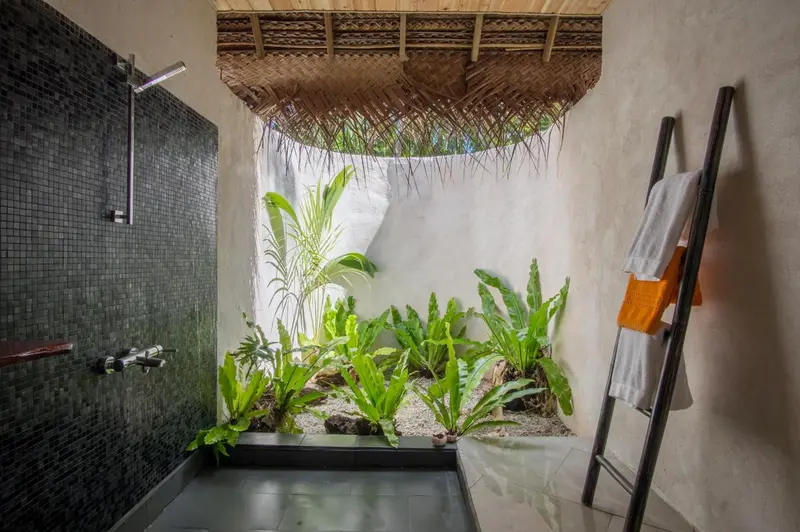 Douche à l'extérieur avec végétation luxuriante et serviettes colorées.