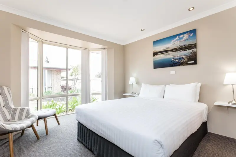Une chambre lumineuse avec un grand lit et un coin salon près de la fenêtre.