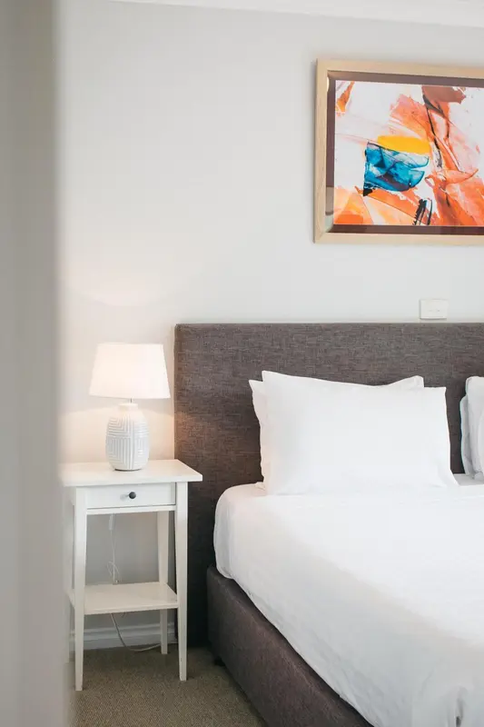 Une chambre lumineuse avec un lit recouvert de draps blancs et une lampe de chevet.