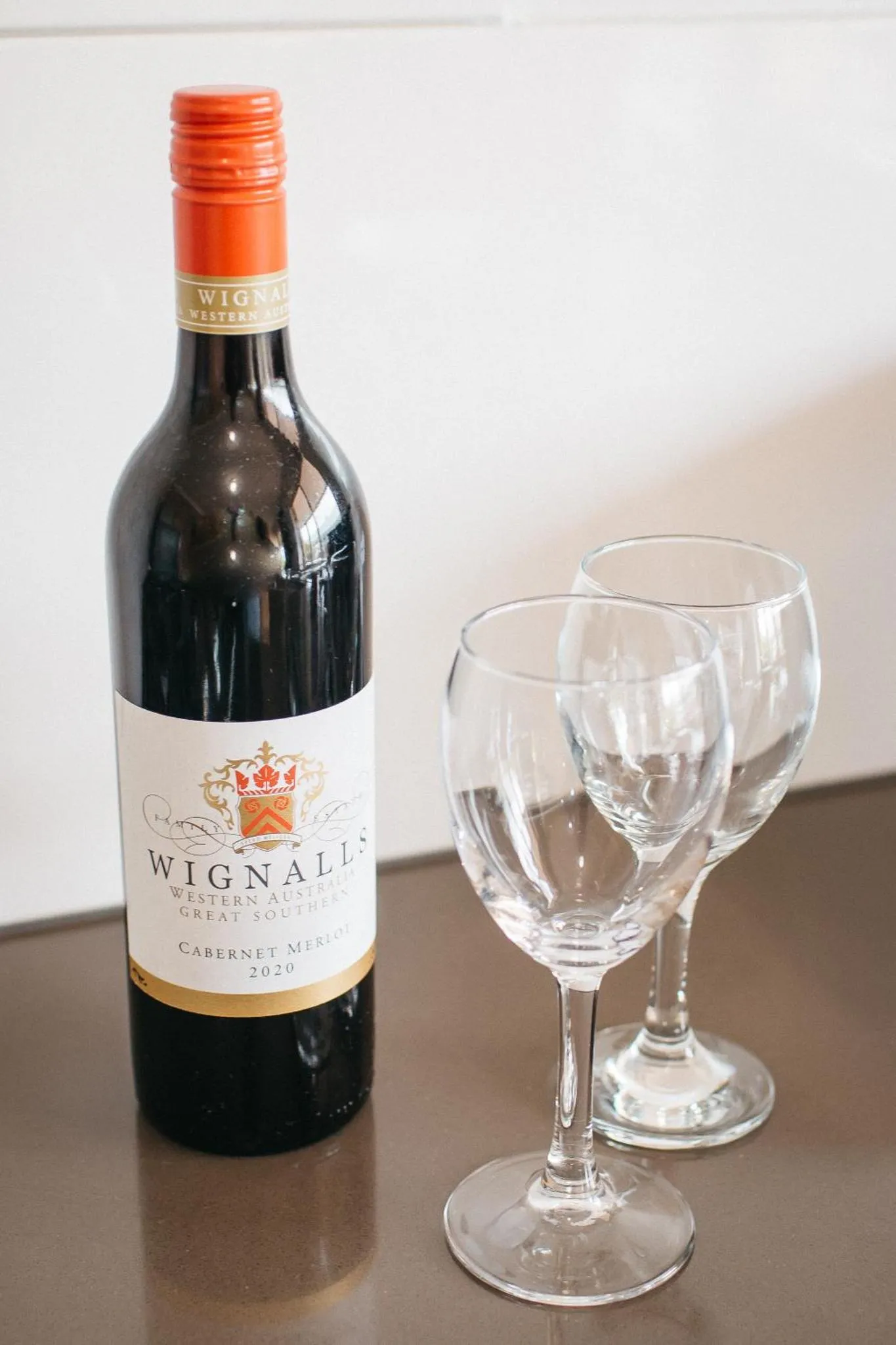 Une bouteille de vin rouge et un verre vide sont posés sur une surface sombre.