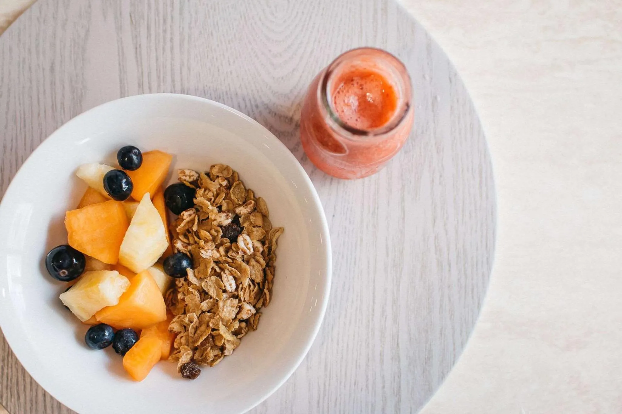 Un bol de céréales aux fruits et un smoothie sont présentés sur une surface claire.