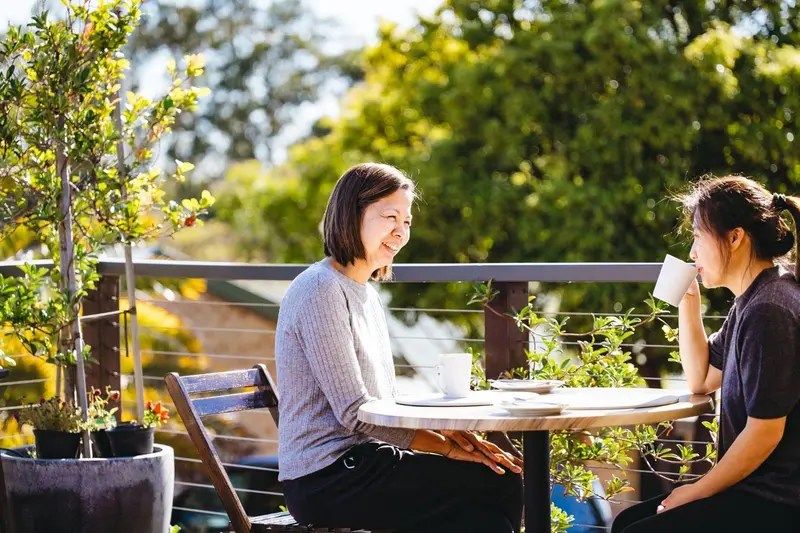 Deux femmes discutent autour d'une table sur une terrasse ensoleillée.