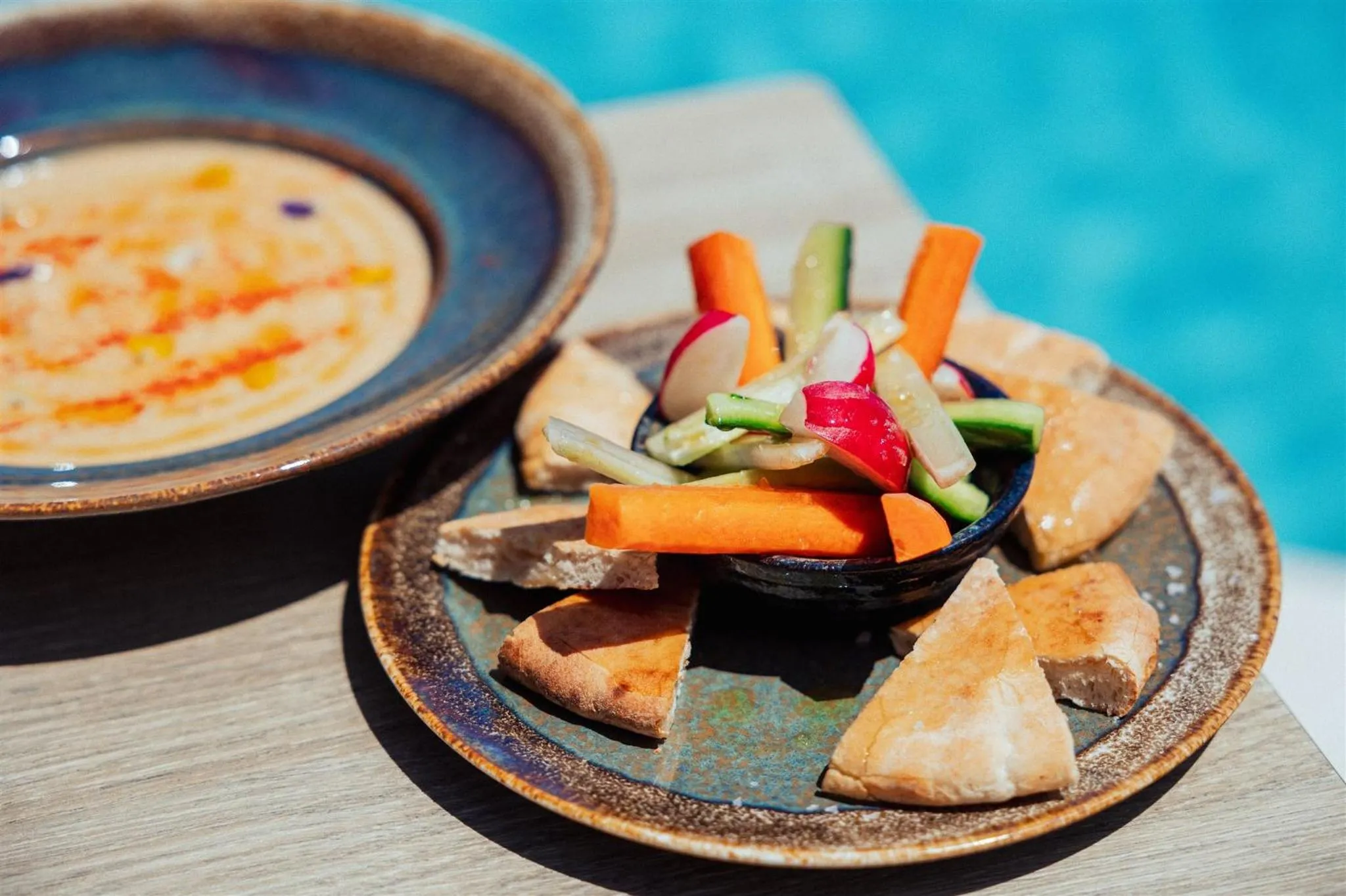 Assiette de houmous, de légumes frais et de pain pita sur une table en bois.