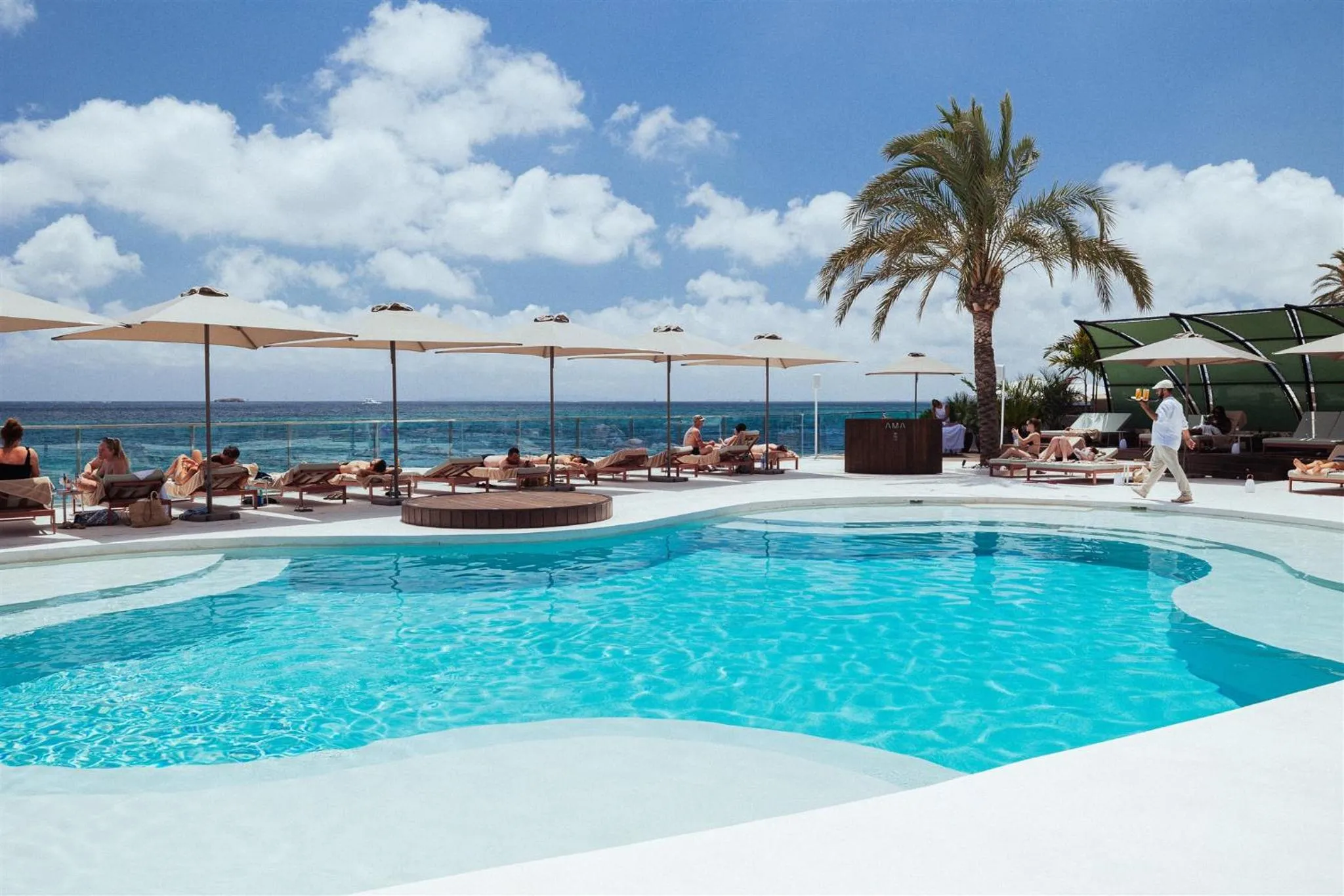 Une piscine bordée de transats sous des parasols, avec une vue sur la mer.