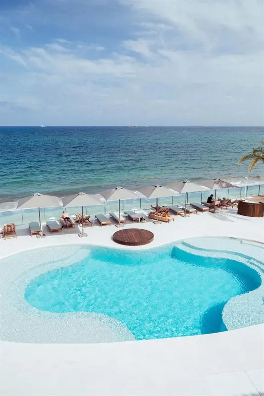 Piscine d'hôtel avec vue sur la mer et transats.