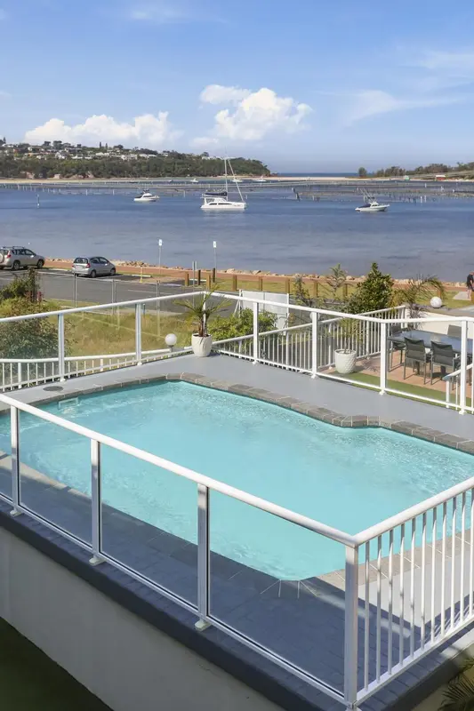 Une piscine rectangulaire avec une terrasse ensoleillée surplombe une baie.