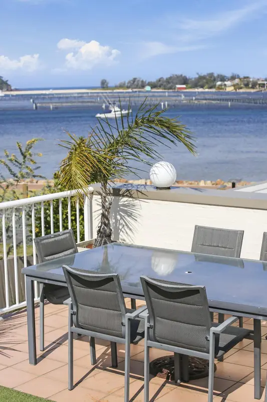 Table et chaises sur une terrasse ensoleillée avec vue sur la mer.