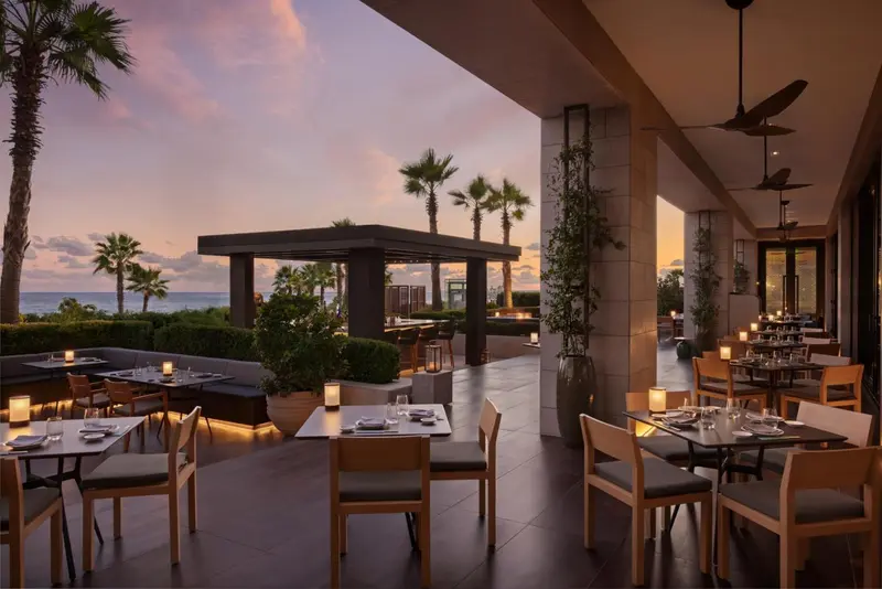 Terrasse de restaurant avec tables dressées face à la mer au coucher du soleil.