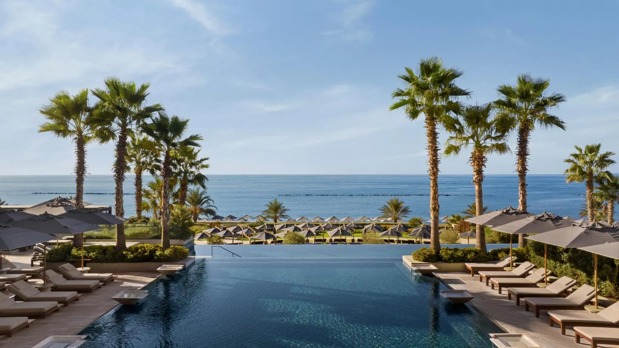 Une piscine à débordement offre une vue sur la mer et une plage bordée de palmiers.