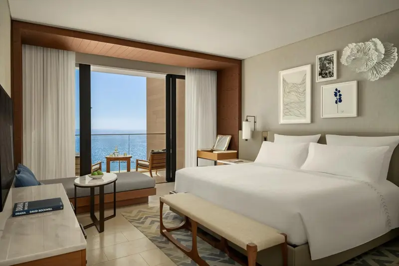 Chambre lumineuse avec un grand lit et une vue sur la mer depuis un balcon.