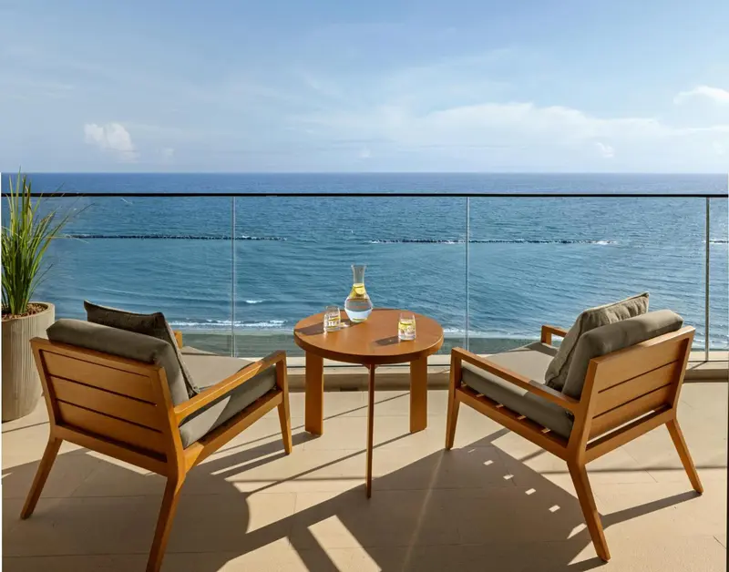 Deux fauteuils en bois et une table basse sur une terrasse avec vue sur la mer.