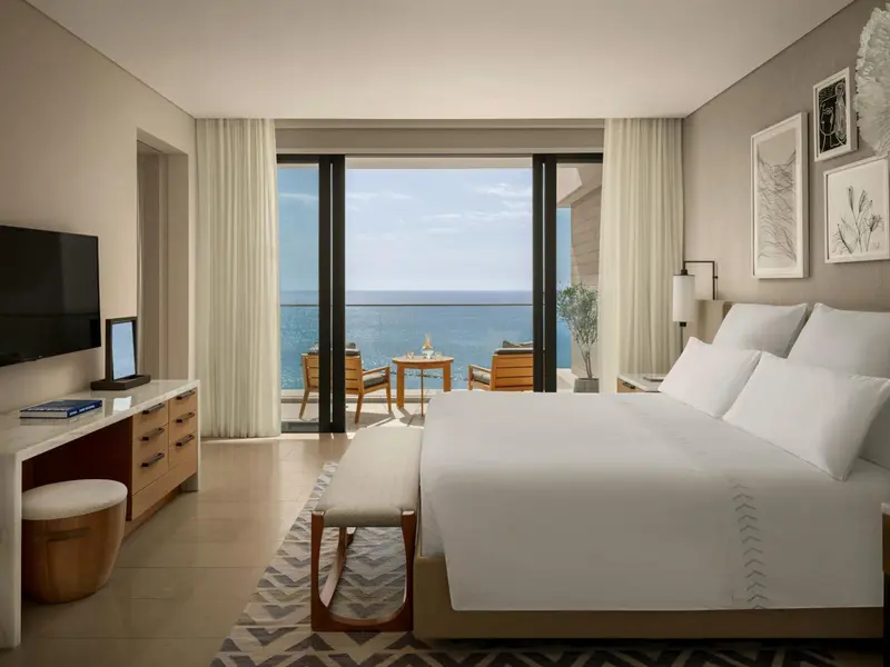 Une chambre lumineuse avec un grand lit et une vue sur la mer depuis un balcon.