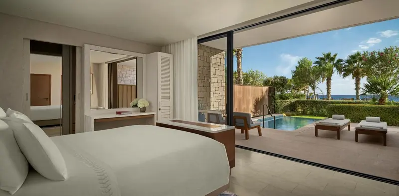 Une chambre lumineuse s'ouvre sur une terrasse avec piscine et végétation luxuriante.