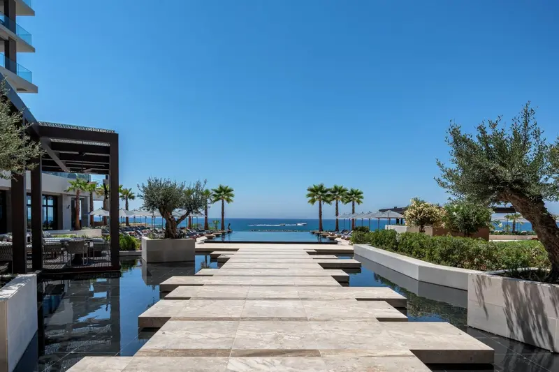Une piscine rectangulaire s'étend vers la mer sous un ciel bleu clair.